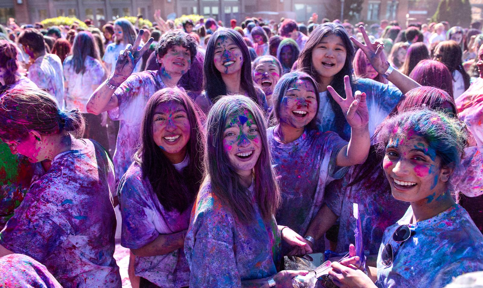 Group of students on a field celebrating Holi and covered in paint